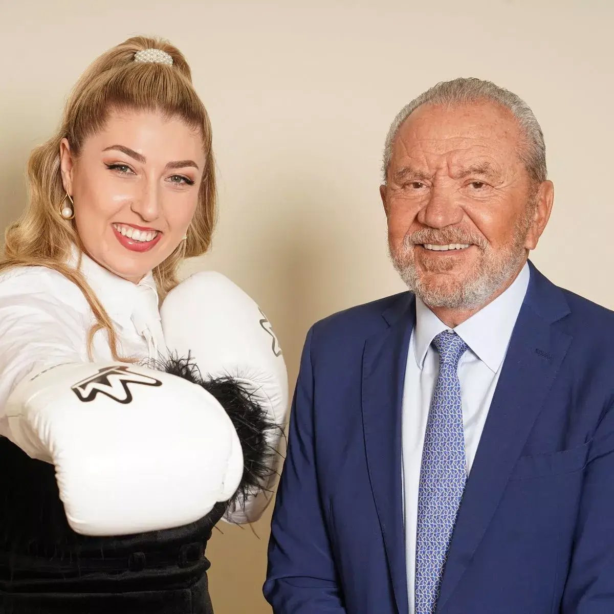 Bronx Boxing is a client of LoudLocal, this image shows Marnie Swindells the founder of Bronx wearing a white shirt and white boxing gloves stood next to Lord Allan Sugar who is wearing a blue suit after she won the BBC's Apprentice.