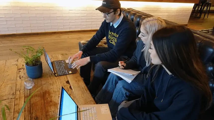 team meeting in café with laptops and the team focusing on one laptop whilst someone is taking notes