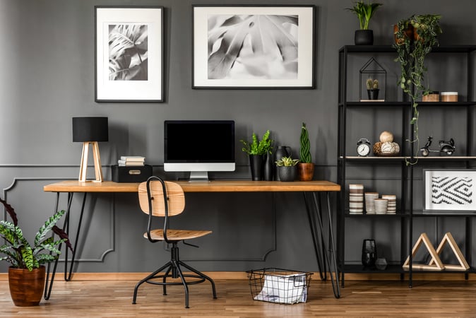 A home office with a wooden desk, computer, chair, shelving and plants.