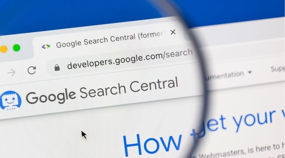 A magnifying glass highlighting the Google Search Central website on a computer screen, with a blue background and the Google Search Central interface visible.