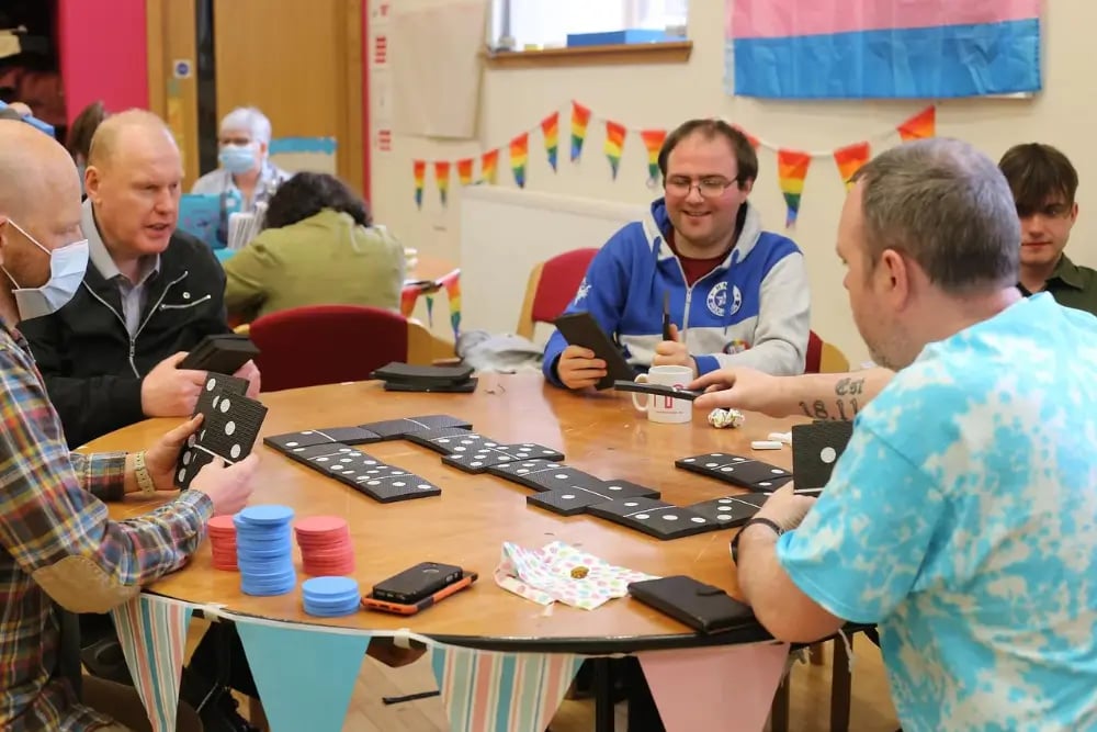 The Action Group is a client of LoudLocal. This image shows a group of people at the Action Group's support centre sat round a table laughing whilst playing dominos. 