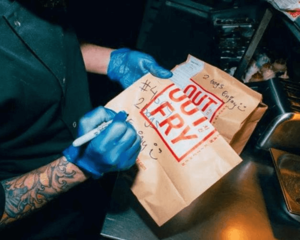 An image from one of Taster's brands 'Out Fry'. Somebody holding an OutFry bag and writing on it