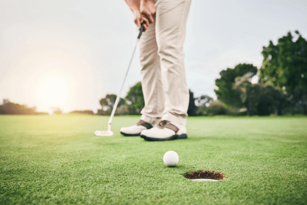 This image shows a golfer putting a ball into a hole. 