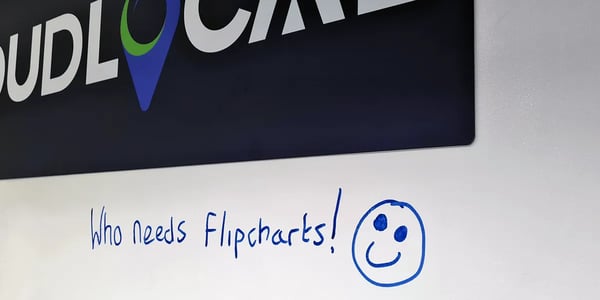 A photo of blue writing on a white wall saying 'Who needs flip charts!' with a smile afterwards.
