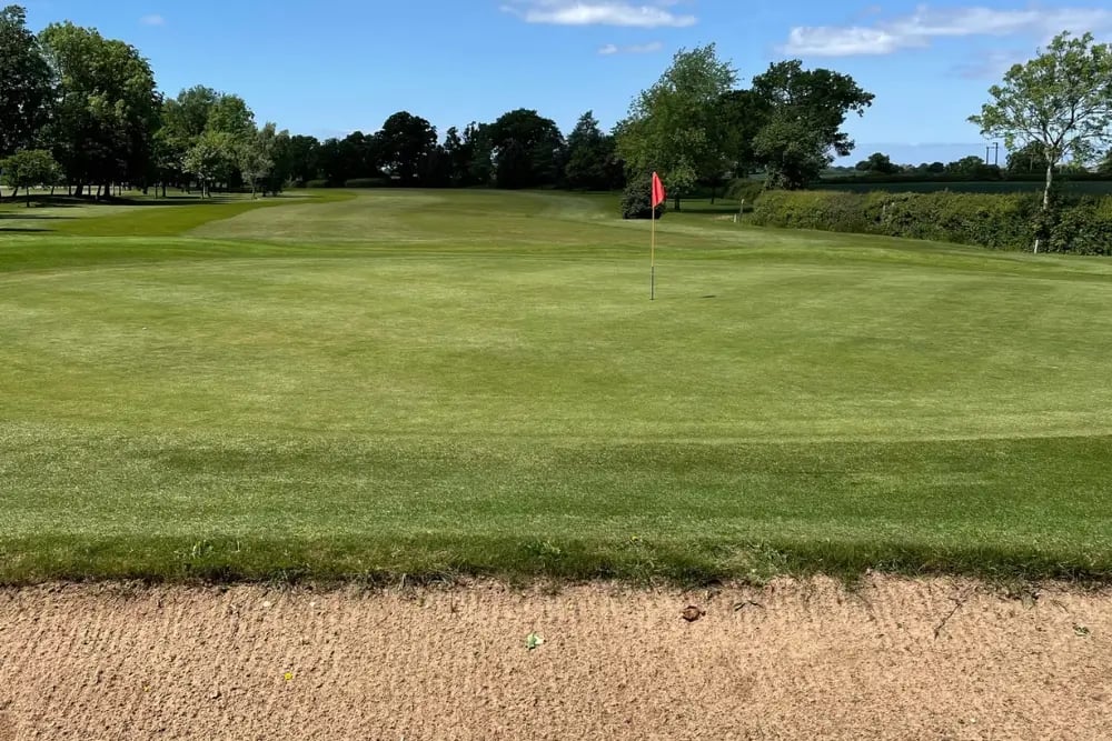 Golf putting green at oakridge golf club one of our clients with bunker in the forefront of the image and trees and blue sky in the background