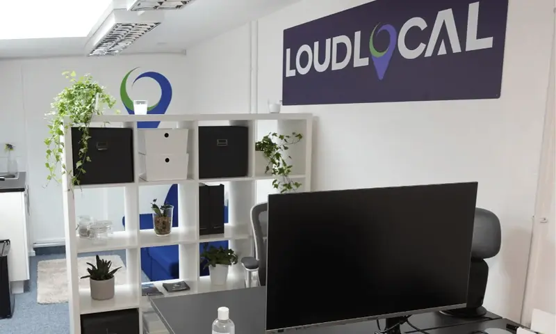 LoudLocal’s former Kenilworth office, with a desk, computer screen, shelving, plants and the old LoudLocal wall sign.