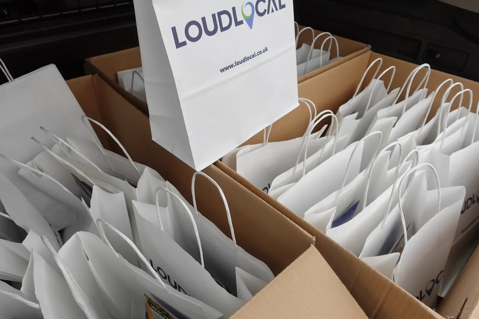 White LoudLocal-branded paper bags packed into cardboard boxes.
