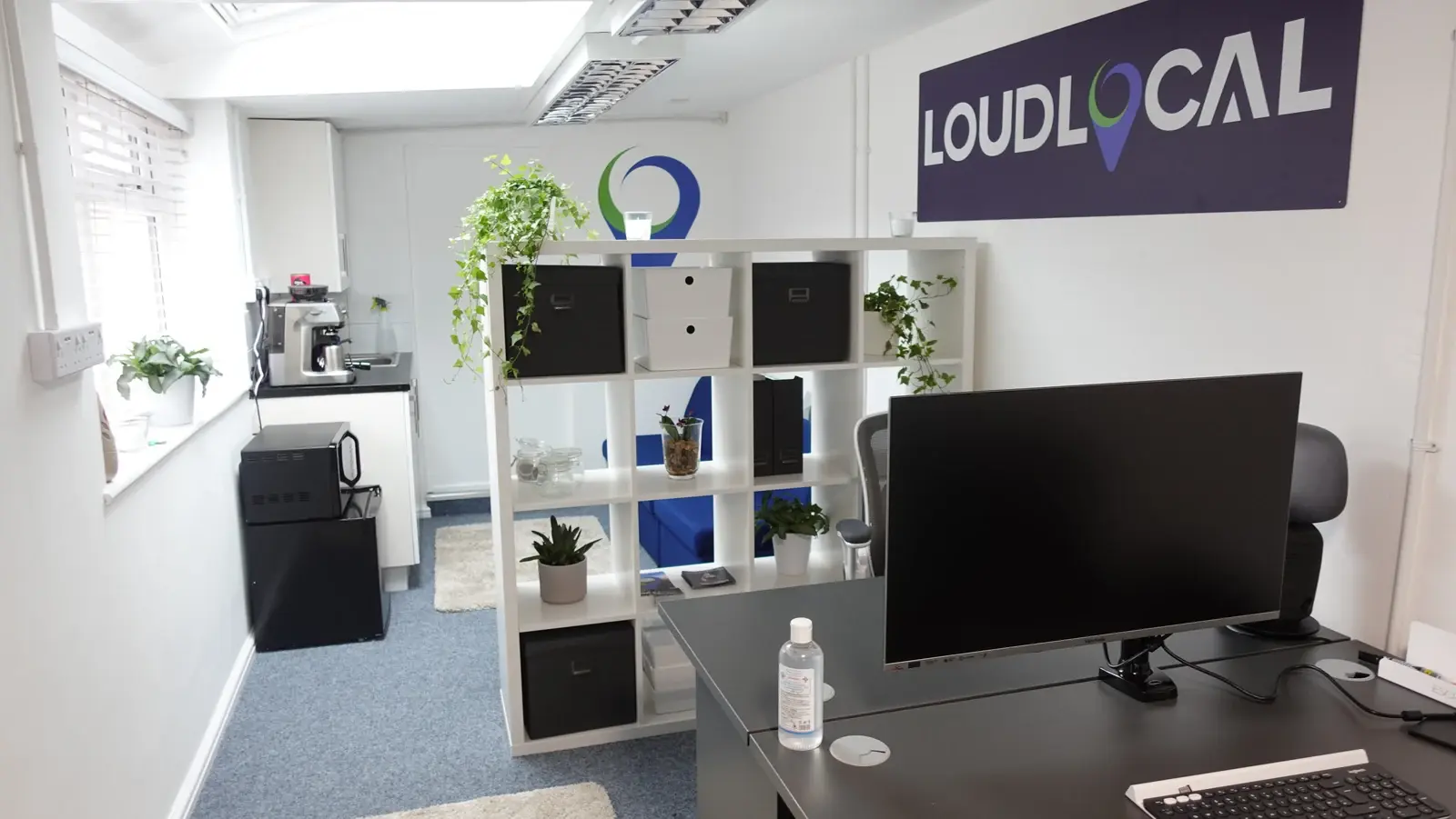 The LoudLocal office with desks, plants, shelving and a wall sign.