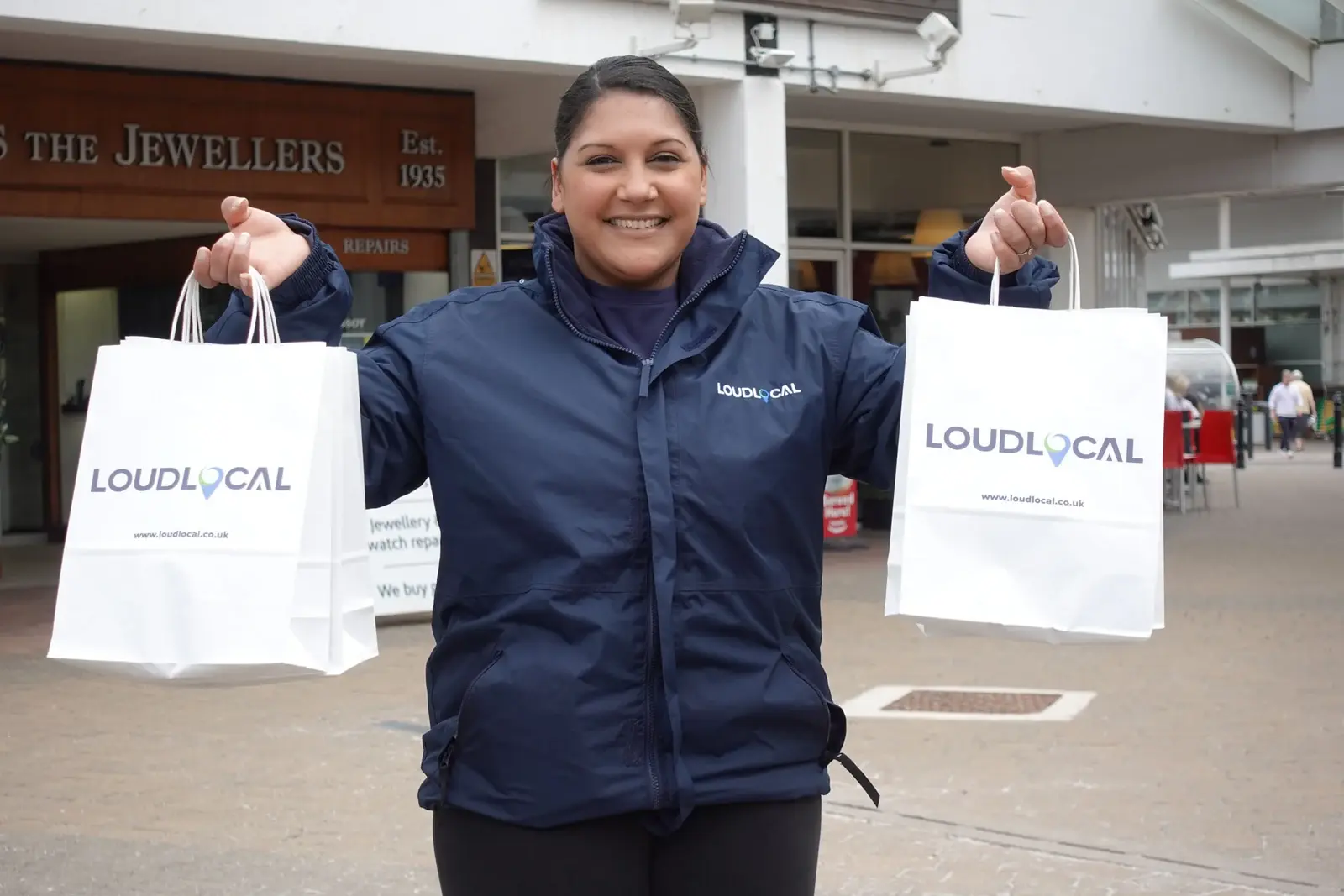 Priya holding two LoudLocal-branded bags outside shops.