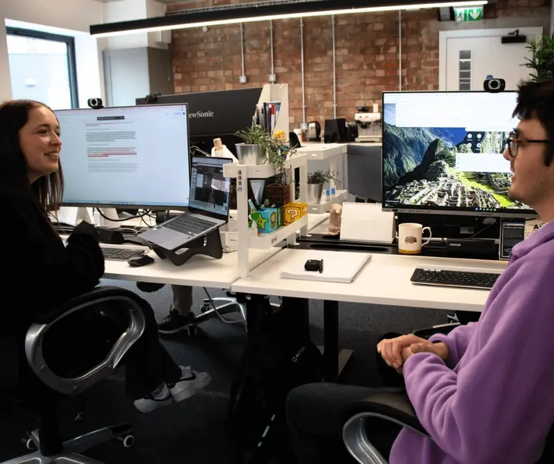 Mia and Toby talking across desks and computer screens in the LoudLocal office.