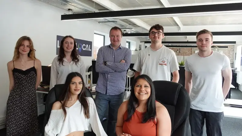 Seven LoudLocal colleagues posing together between desks in our new Leamington Spa office.