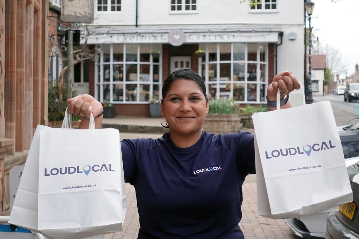 Priya, LoudLocal’s Commercial Director, holding two LoudLocal-branded bags outside a shop in Kenilworth town centre.