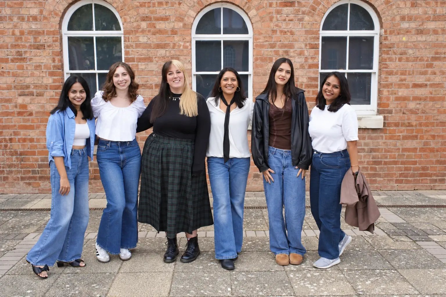Siddhi, Mia, Andrea, Priya, Tanya and Natasha standing together outside a brick building.
