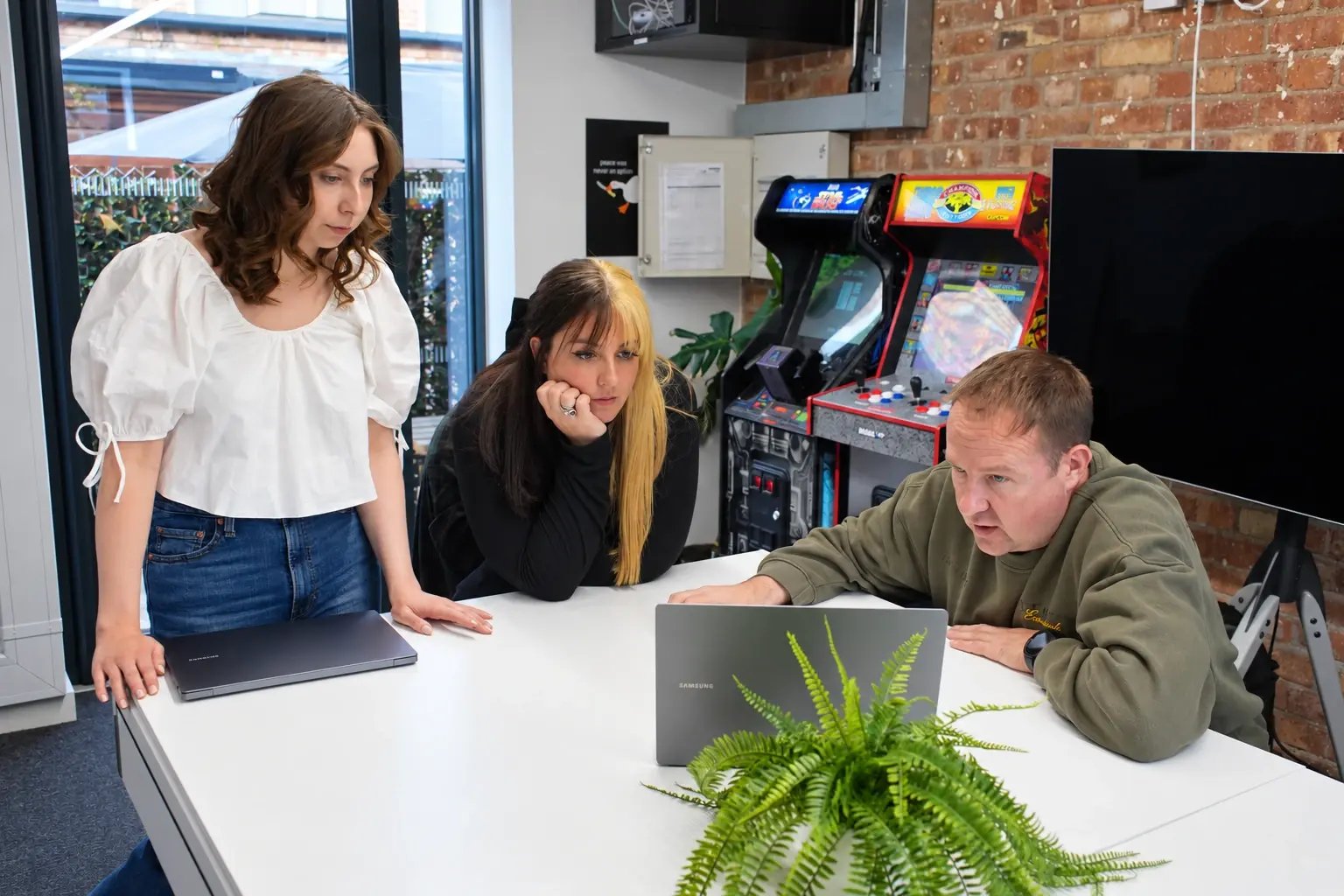 Mia Deeming, Andrea Thomas and Leon Hidderley discussing work around a laptop in LoudLocal's gaming room.