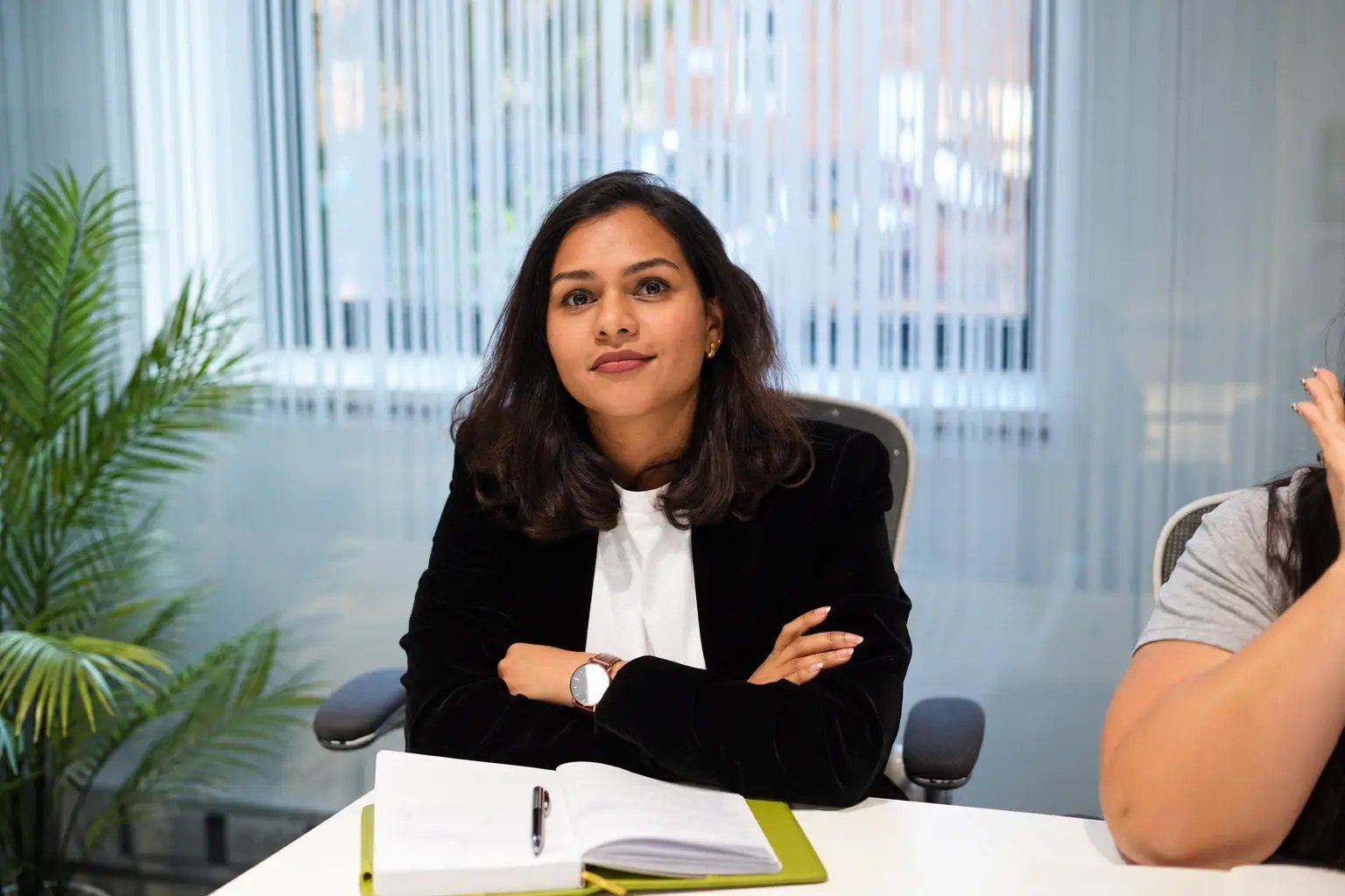 Natasha D'souza seated in a meeting with an open notebook.