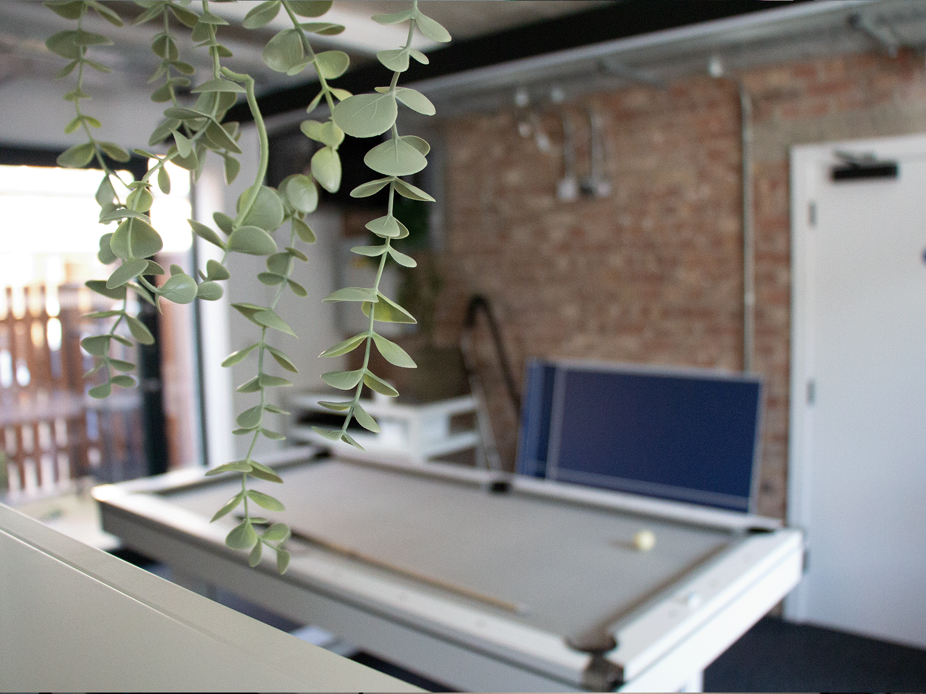 The new office has a pool table. There is a red brick wall in the background, the pool table is white and grey. 