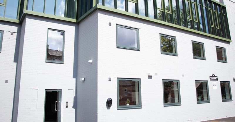 LoudLocals new office in the heart of leamington spa. The building is grey with green window frames and a door with a matching frame. It is a sunny day and blue sky can be seen in the background.