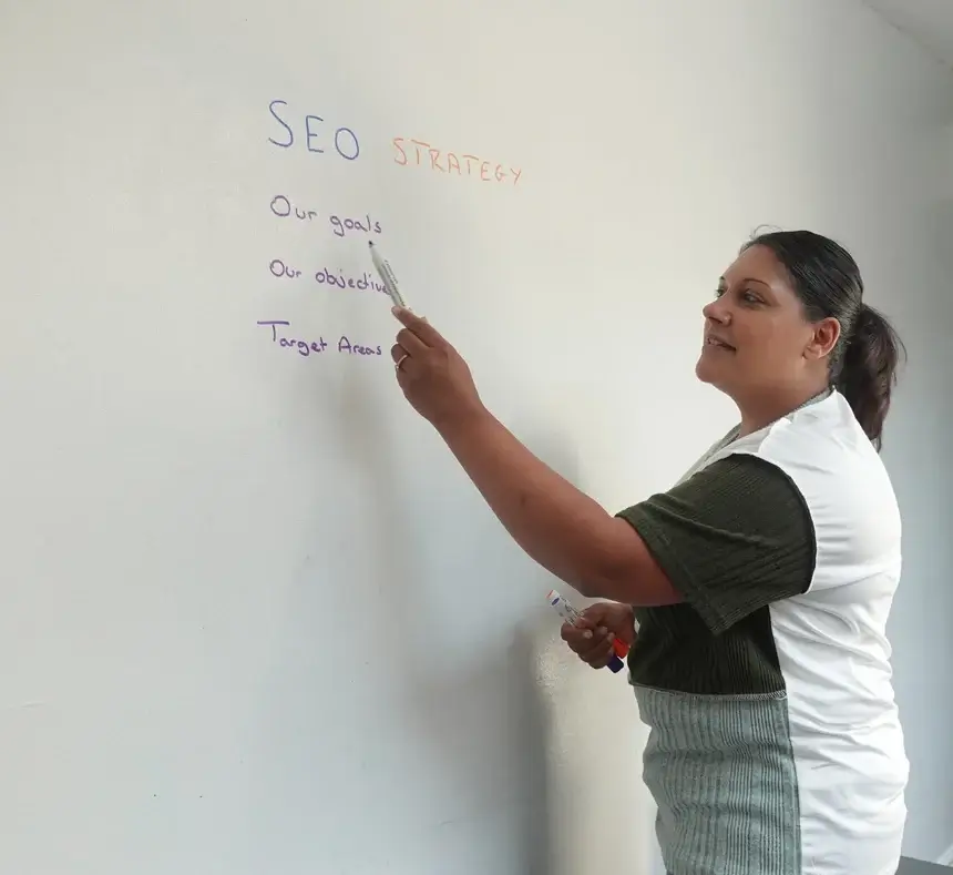 Priya our Commercial Director, consulting with a client on search optimisation strategy.  Priya is wearing a white top, with dark sleeves and writing on a wall 