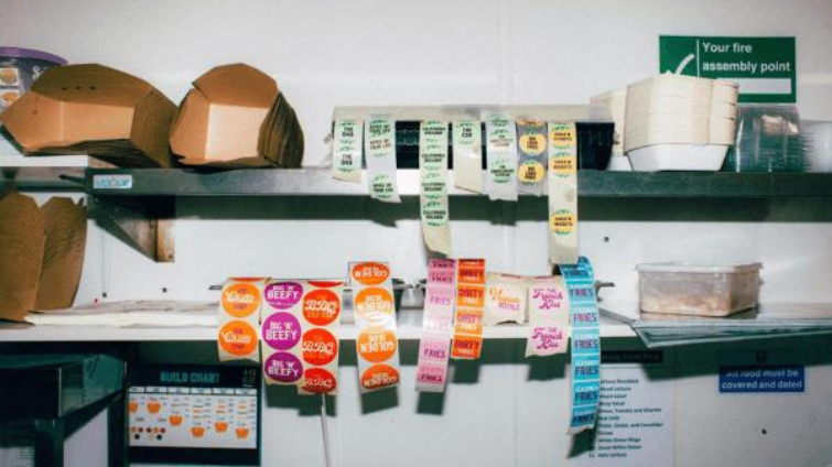 Taster is one of LoudLocal's clients, the image shows the stock room of one of the franchise kitchens, with brown takeaway boxes stacked on shelves as well as branded stickers and signs on the wall.